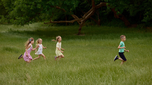 Children running through grassy field in park. Concept of active play, outdoor education, wellness programs, family services and healthy lifestyle promotion.