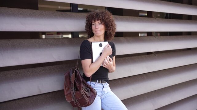 A young woman with curly hair is confidently standing against impressive modern architecture