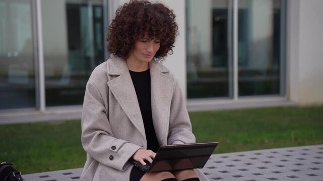 A young professional is working on their laptop outdoors, surrounded by greenery and sunshine
