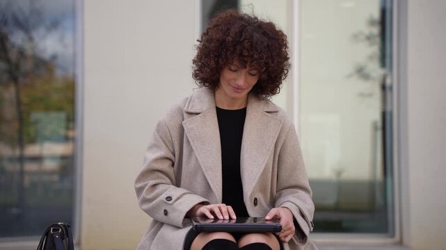 A Professional Woman Relaxedly Sitting Outdoors, Engaged with Her Tablet Device Today