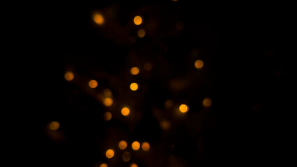 Fototapeta premium Light bokeh forming warm golden glowing dots on deep black background with soft blur. Light creating dreamy abstract illumination pattern, festive sparkle mood, night decoration concept, texture