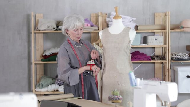 Attentive mature female dressmaker working with tailor's dummy in sewing workshop
