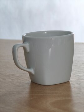 Side view of empty white ceramic mug on wooden table with blurred background