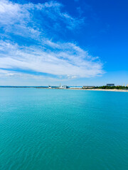 Fototapeta premium Clear blue water and sky over the harbor with boats and buildings in the distance during daytime