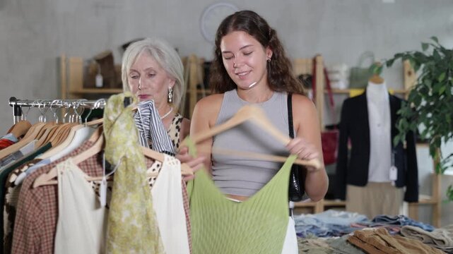 Two happy women of different ages choose summer clothes in a fashion boutique. High quality 4k footage