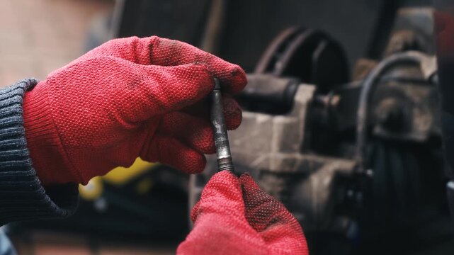 Inspecting caliper guide pin for wear and damage with gloved hands during vehicle maintenance. Automotive repair concept with closeup component check, disc assembly servicing and mechanical inspection