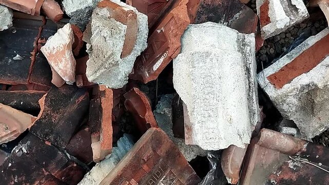 High angle close up focusing on a large concrete block mixed with broken roof tiles shifting slightly.