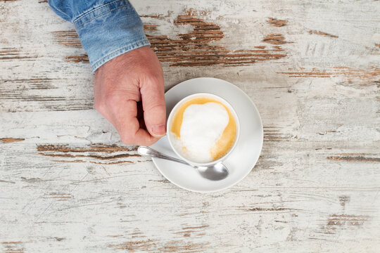 Una mano de un hombre sosteniendo una taza de cafe con leche sobre una mea de madera. Vista superior y de cerca. Copy space