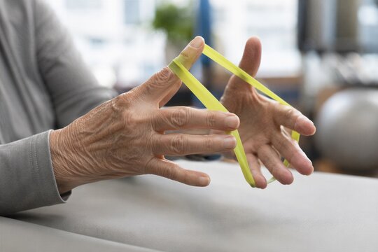 Elderly person performing hand exercises with resistance band, focusing on therapy for aging hands and fingers