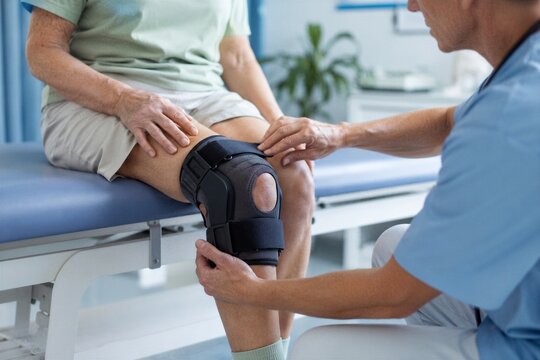 Doctor adjusting knee brace on elderly woman leg. Arthritis treatment and rehabilitation concept. Medical clinic examination for senior health care
