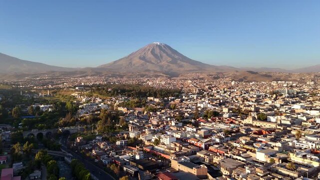 An aerial flyforward shot moves toward the snow-capped peak of El Misti volcano towering over the sprawling urban valley of Arequipa, Peru