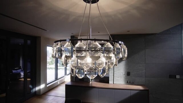 Panning camera revealing crystal chandelier above kitchen island, showcasing modern open plan space