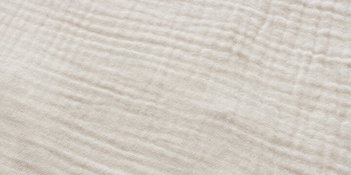 Top view close up of soft crinkled beige muslin fabric texture. Light double gauze cotton textile background with copy space