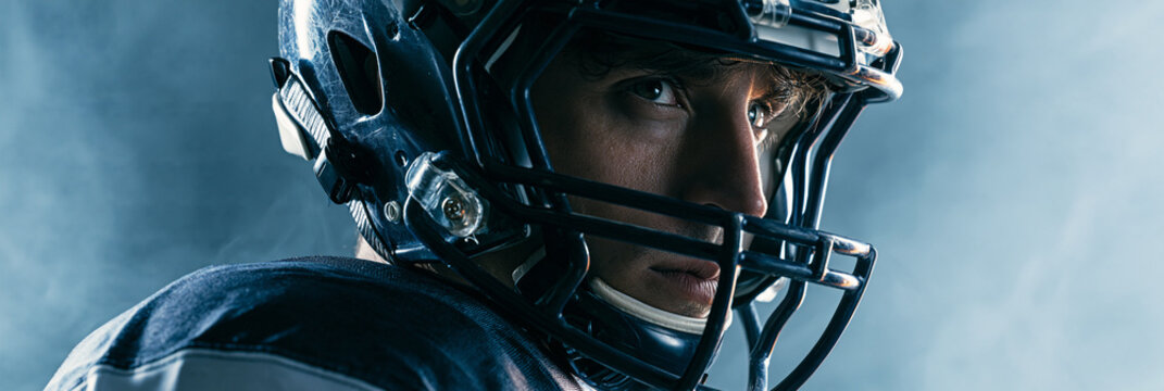 Focused male athlete in a football helmet with an intense gaze and dramatic lighting.