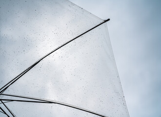 Transparent umbrella covered with raindrops against a cloudy sky, Rainy weather, protection, climate change, safety, resilience, seasonal rain, and storm preparedness. © Lahmz