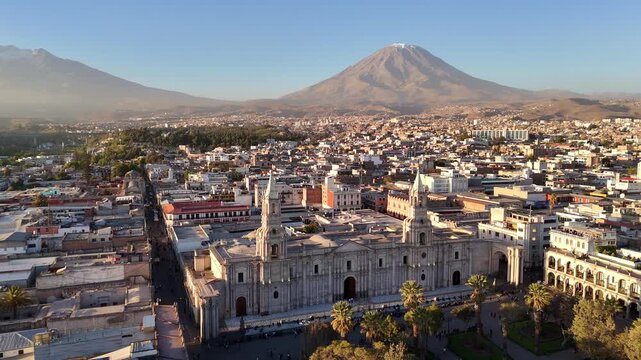 An aerial close-up shot rotates to the left around the twin towers of the Basilica Cathedral in Arequipa, Peru, from El Misti and revealing the Chachani volcano.