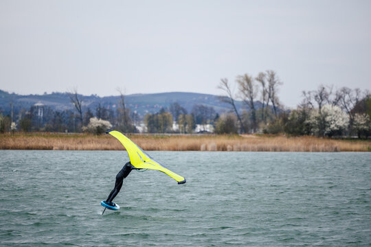 Aquatic sport wing foiling on windy lake. Wingfoiler balancing on hydrofoil board with inflatable wing