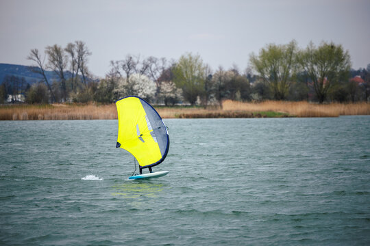 Wingfoiler riding foilboard on windy lake. Extreme water sport wing foiling