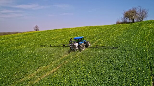 A drone view shows a tractor-mounted sprayer working on green farmland, performing agricultural spraying for crop protection, field maintenance, and modern farming practice.
