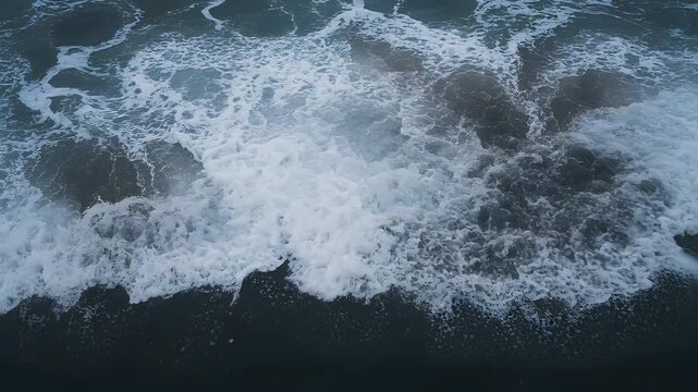 Breaking surf zone pushing incoming swell onto dark wet sand, forming cellular foam patterns