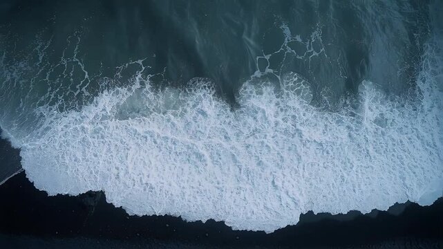 Surging ocean swell crest collapsing onto dark shoreline, creating lace-like whitewater and foam
