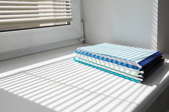 There is stack of documents on windowsill. Accounting. Shadow of blinds on the windowsill. Documents and notebooks for notes. Concept of office management and accounting. Place to copy