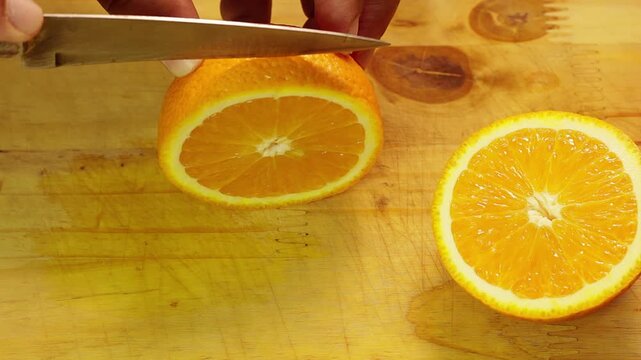 Knife cutting slices of fresh orange on a wooden board in a diner kitchen