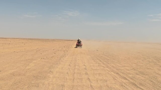 Cinematic rear view of a convoy of tourists riding quad bikes along a remote desert road, leaving a trail of dust behind. Freedom, adventure and exploration. 