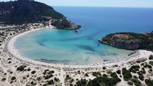 Drone view of the iconic Voidokilia Beach in Messinia, Greece, featuring a semicircular sandy bay, turquoise waters, coastal dunes, and pristine Mediterranean scenery.