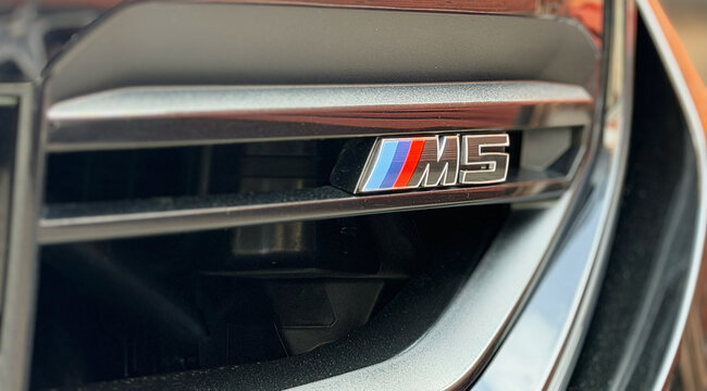 BMW M5 VII G90 badge on the car&rsquo;s grille, highlighting the iconic branding and sleek design in a showroom setting. BMW M5 VII G90 logo on black car. Hood, black kidney grille. Emblem of BMW M5. 