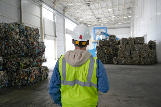 Worker in reflective vest and white helmet inspects a warehouse for sorting plastic waste pressed into briquettes