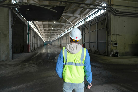 Person in hard hat and safety vest faces away, looking down a long, dark industrial garbage facility hall