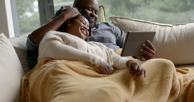 African-American couple on couch, camera pulling back, man cradling her head holding tablet viewing