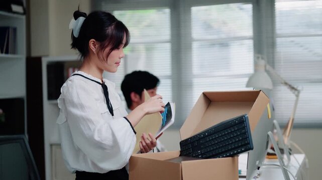Asian Businesswoman Packing Personal Belongings in Cardboard Box After Being Sacked from Office Job