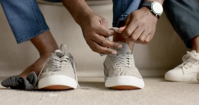 Couple sitting at home entryway, man tying light gray sneakers while preparing to leave