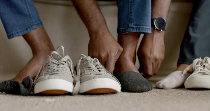 African couple on couch, man pulling on sock then sliding foot into sneaker, preparing to leave