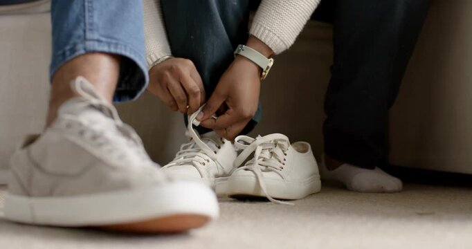 Couple on couch watching woman reaching and tying white canvas sneaker after spotting loose laces