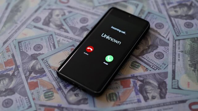 Smartphone showing scam call on screen lying on dollars.