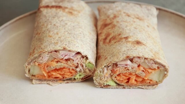 Close-up of a sliced healthy tuna wrap served on a dish, packed with creamy avocado, fresh crisp cucumber, and bright shredded carrots