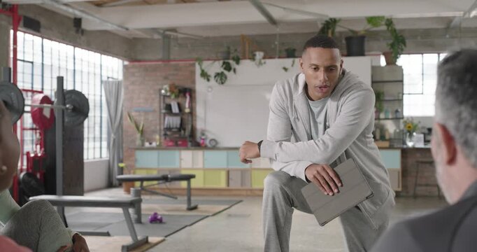 African American male coach entering, crouching on bench, using tablet, debriefing group in studio