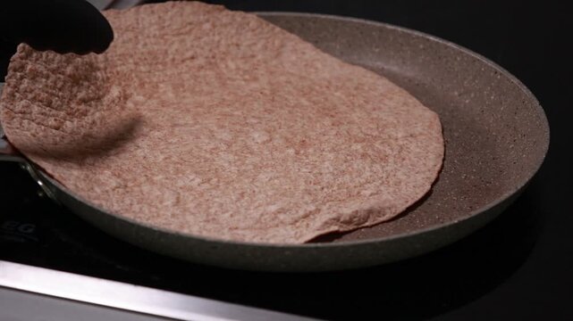 Close-up of heating a fresh plain tortilla flatbread in a hot frying pan until slightly toasted and warm