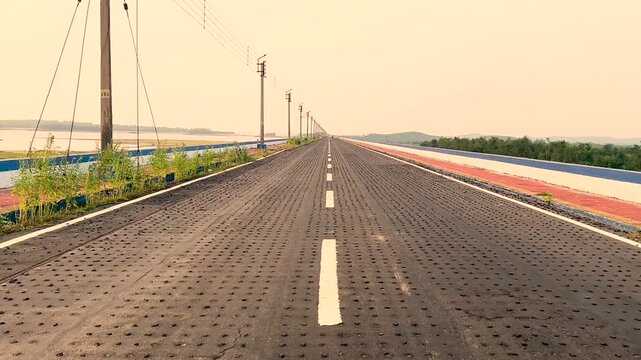 Mukutmanipur Dam In Bankura District West Bengal Straight perspective view of long empty highway road extending towards horizon on concrete dam structure.