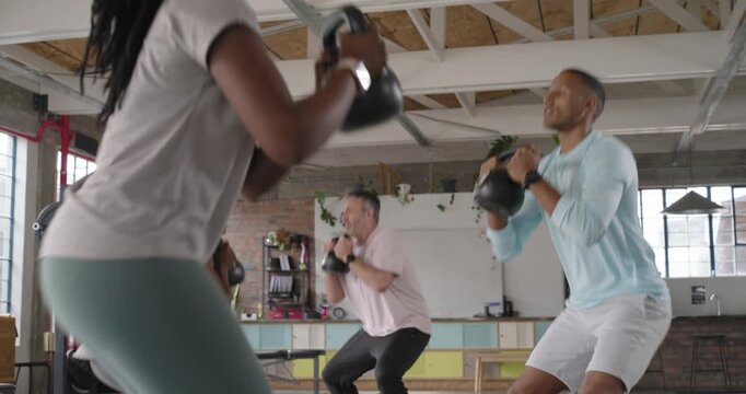 Diverse group of participants on instructor cue, performing kettlebell goblet squats in loft studio