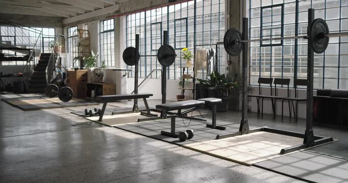 Camera panning right, racks, benches and dumbbells moving center by window light to frame equipment