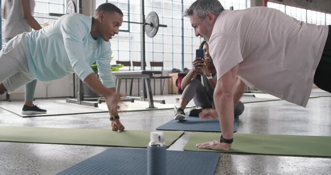 Friends in loft gym doing push-up duel on mats, men touching fists, women filming, huddling phone