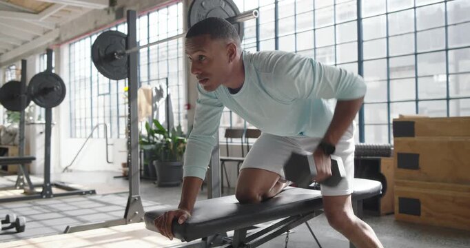 African American man in blue top picking up dumbbell, performing rows on loft bench for strength