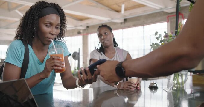 African American women tapping phone on card reader to pay while server presenting at cafe counter