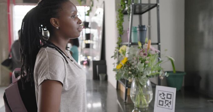 African American woman showing phone for QR scanning at counter, accepting cup, joining friends