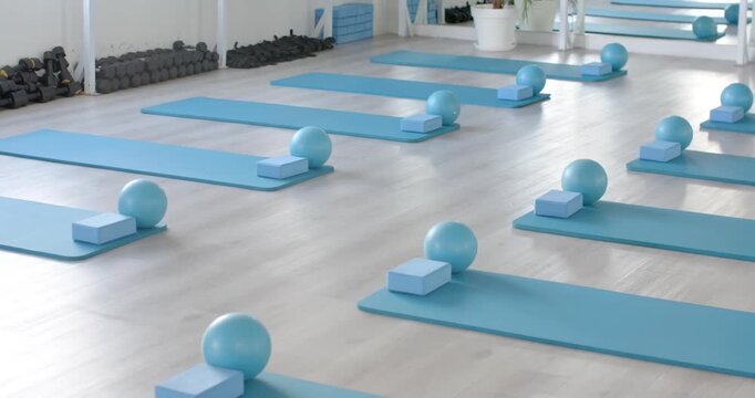 Slider is moving camera diagonally to reveal rows of light-blue mats, balls, blocks in studio