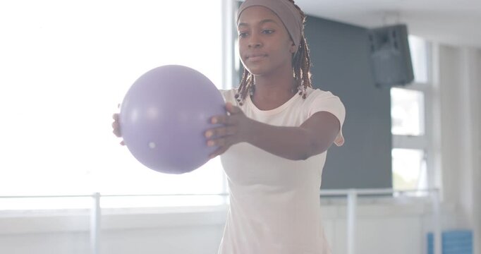 Starting from low squat, adult woman pressing and rotating purple ball for core stability in studio